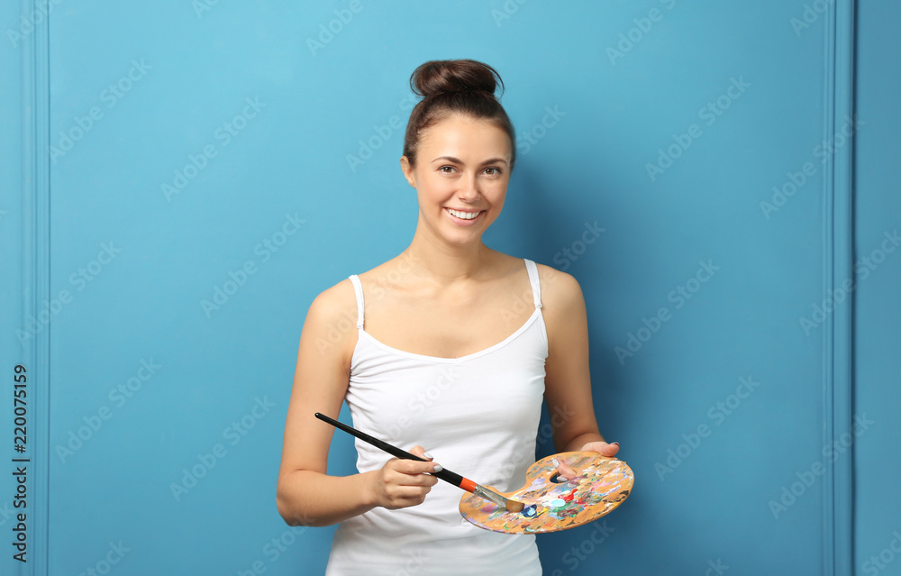 Female artist with brush and paint palette on color background