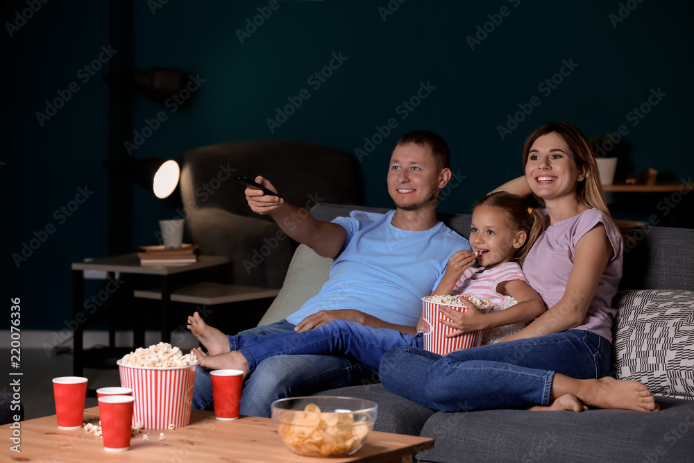 Family eating popcorn while watching TV in evening