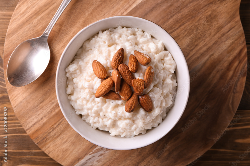 Delicious rice pudding with almonds in bowl on wooden board