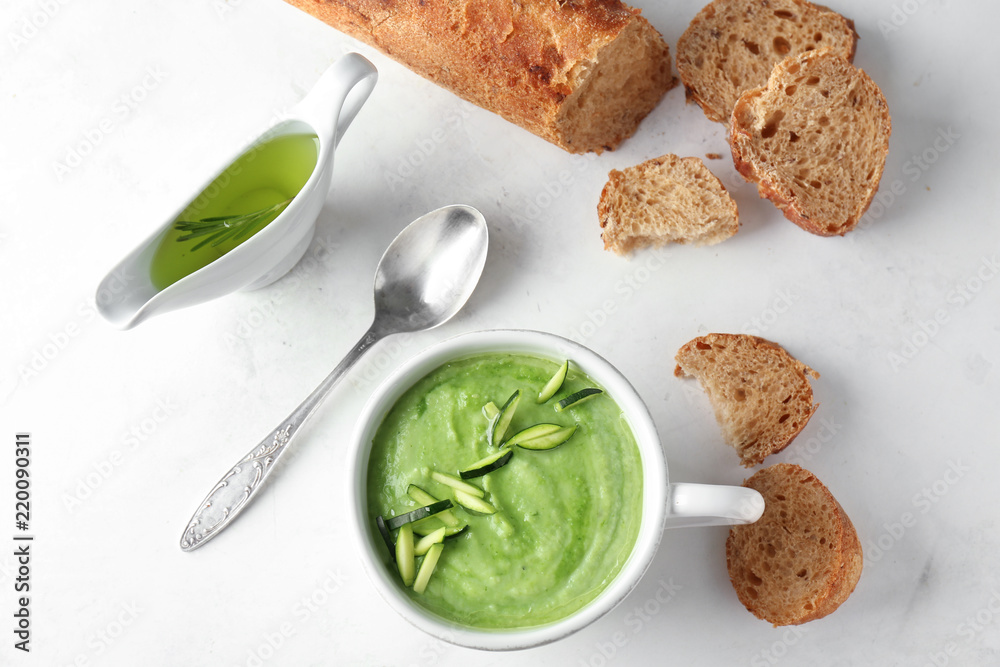 Tasty zucchini soup in cup with bread on light table