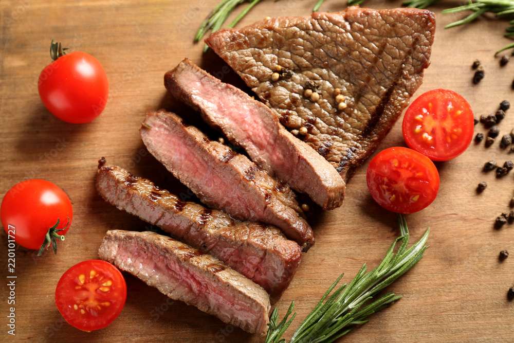 Cut grilled steak with tomatoes and spices on wooden board