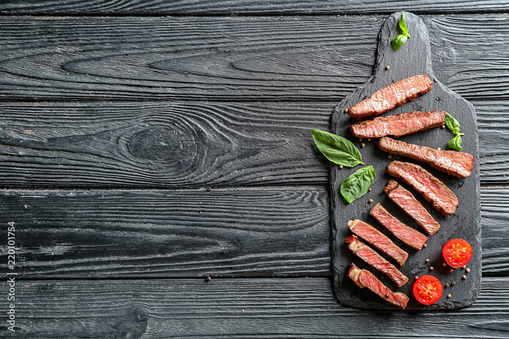 Slate plate with cut grilled steak on wooden table