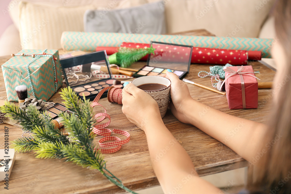 Woman drinking coffee at wooden table with cosmetics and Christmas decorations