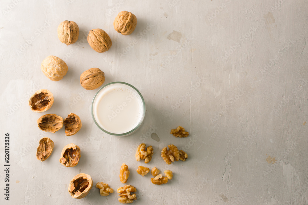 Organic walnut nuts and glass of walnut milk on stone background.