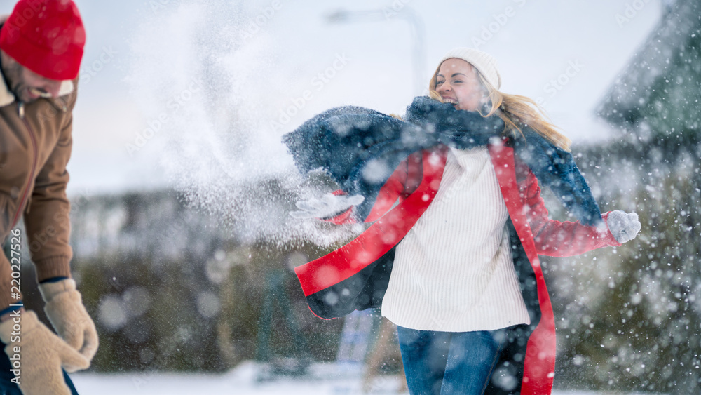 Young Beautiful Couple Throws Snow at Each other While Snow Falls. Happy Man and Woman Playing with 