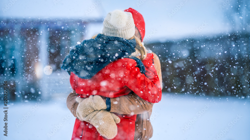 美丽的年轻夫妇在他们田园小屋的后院亲吻，而雪花浪漫地飘落。Hap