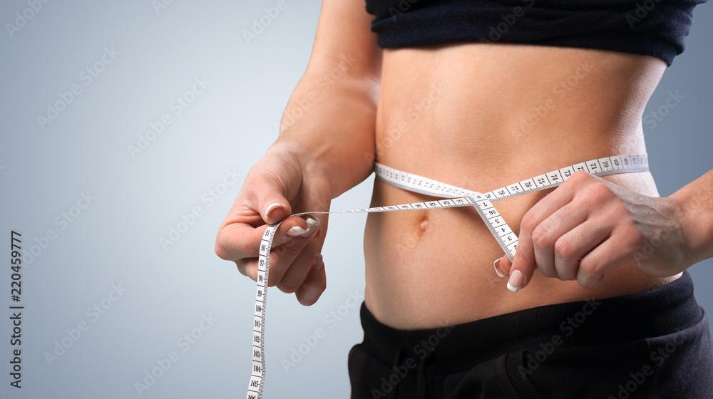 Slim young woman measuring her thin waist with a tape measure