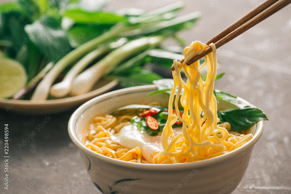 closed up instant noodles with vegetables on chopstick isolated on dảk stone background, junk food o