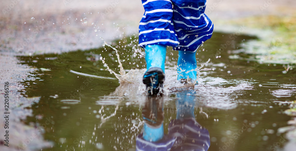 雨天孩子穿着雨鞋在水坑里行走。夏天男孩在雨中