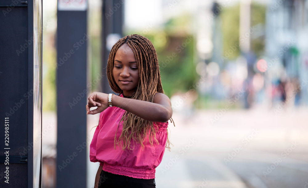 Young African woman checking time and waiting at city bus stop