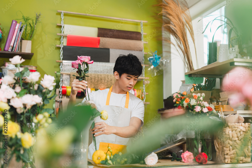 小生意。男花店老板在花店柜台制作玫瑰花束。男助理或其他