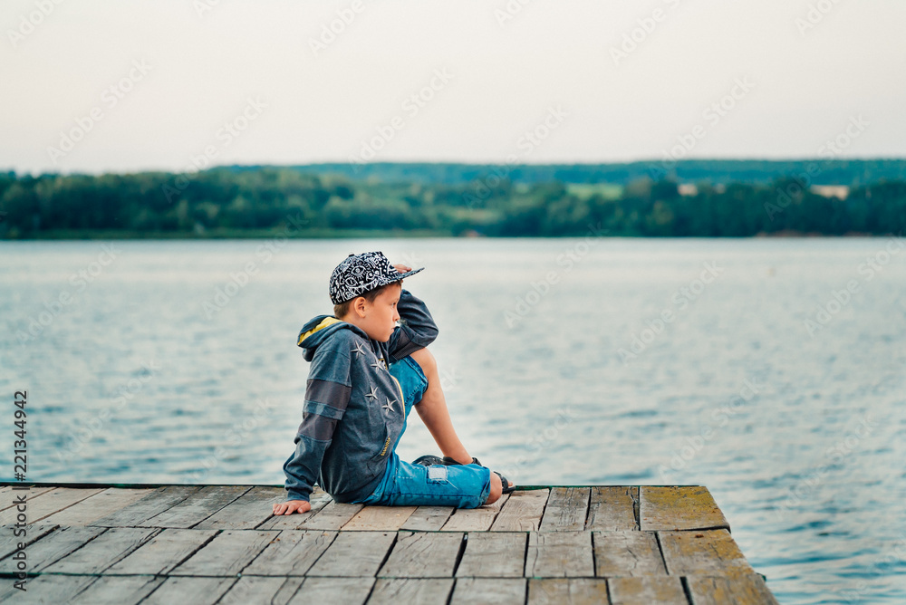 a child in stylish clothes are posing on a photo session on the bridge on the background of the lake