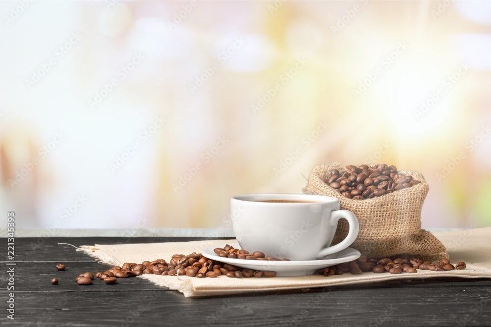 Cup of hot coffee with beans on background