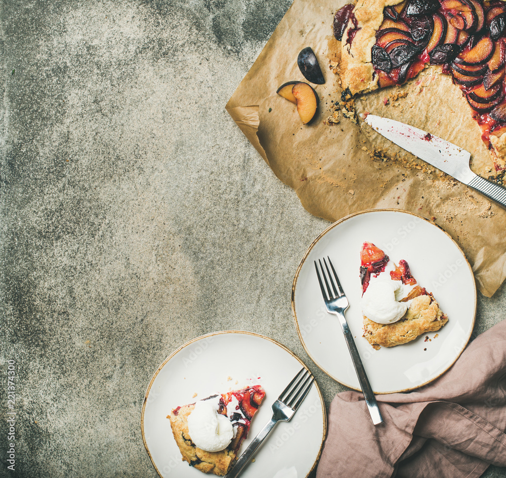 Flat-lay of plum galetta sweet cake in white plates over grey concrete background, top view, copy sp