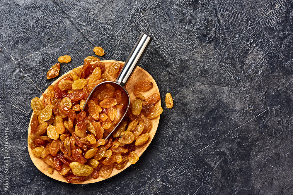 Yellow big raisins on black concrete background with copy space. Top view of dried grapes.