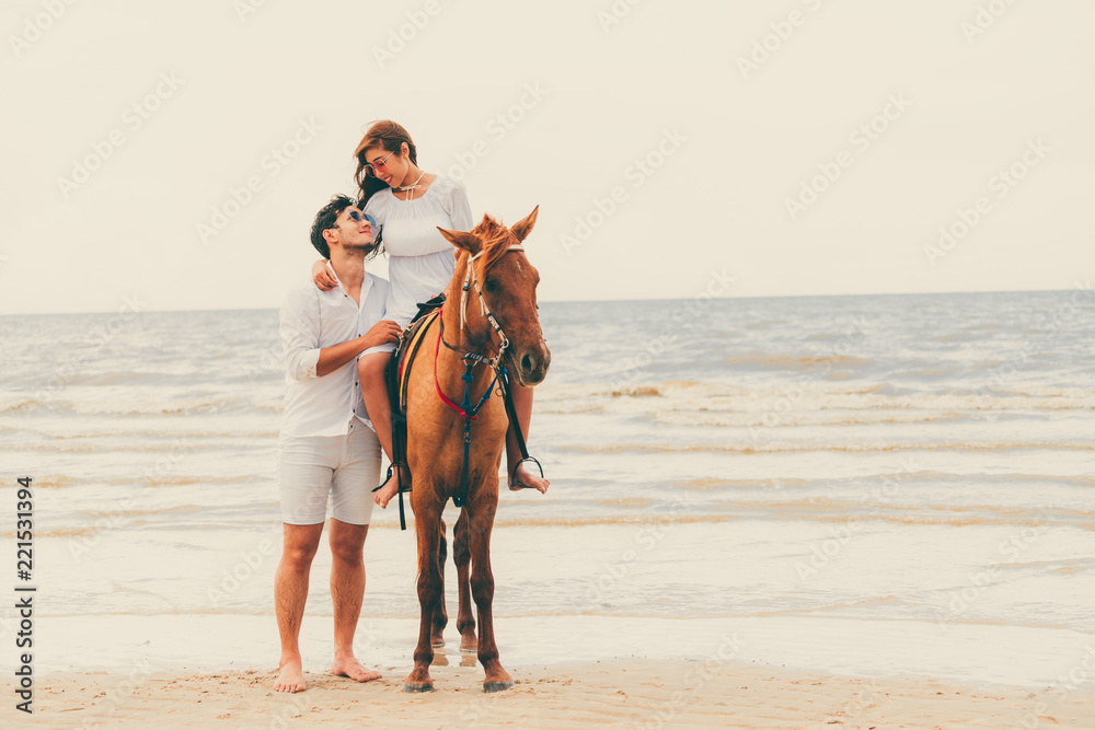 一对年轻夫妇在热带海滩上骑马。