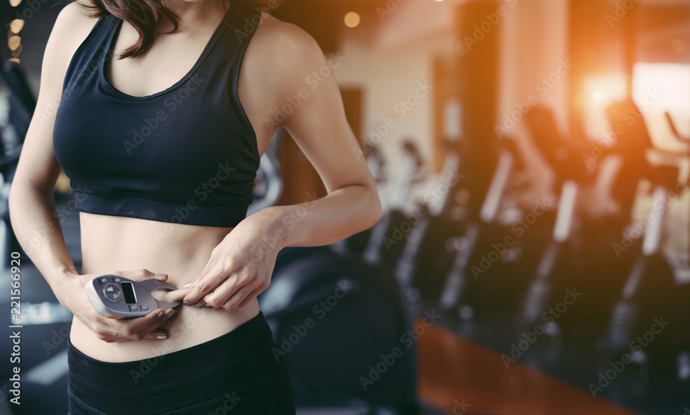 Woman athlete using body fat measurement and waist size with digital caliper after workout at fitnes