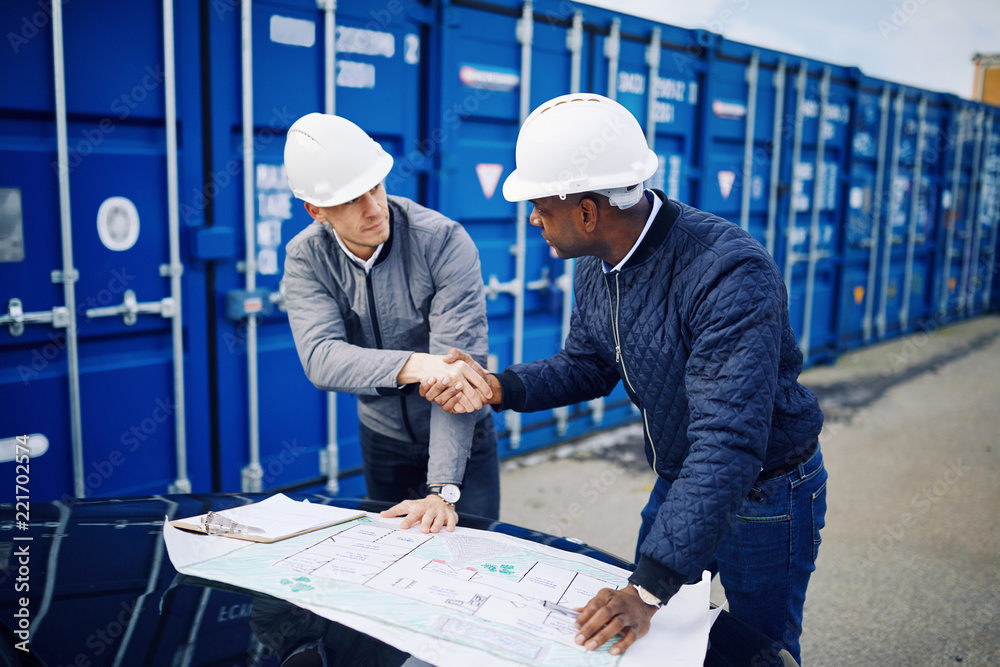 Engineers shaking hands and discussing blueprints in a freight y