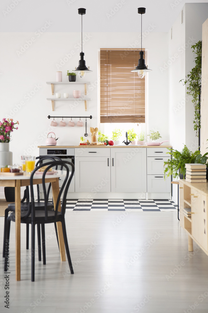 Black chair at table in white open space interior with kitchenette with blinds at window. Real photo