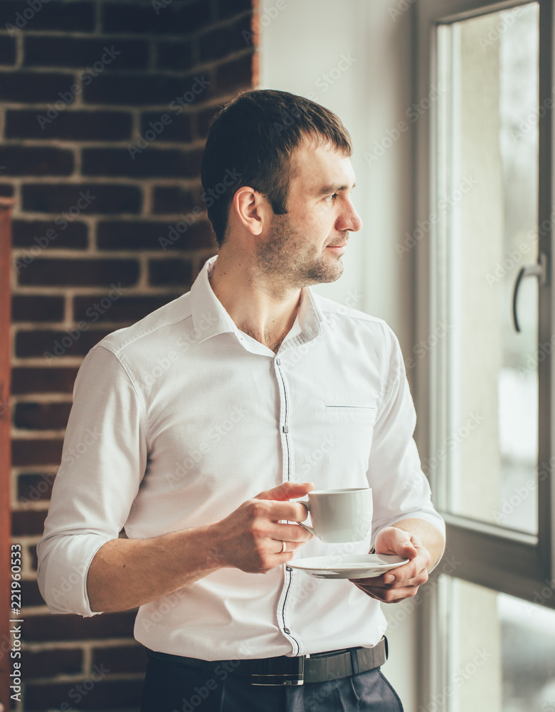 businessman looks in a window with a cup of coffee in his hand from the office. The man observes wha