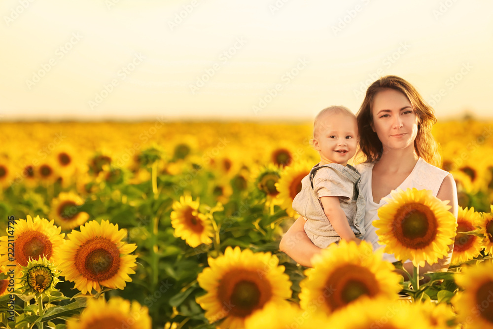 Beautiful woman with her little son in sunflower field on sunny day