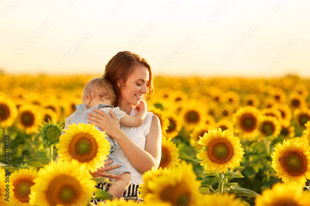 Beautiful woman with her little son in sunflower field on sunny day