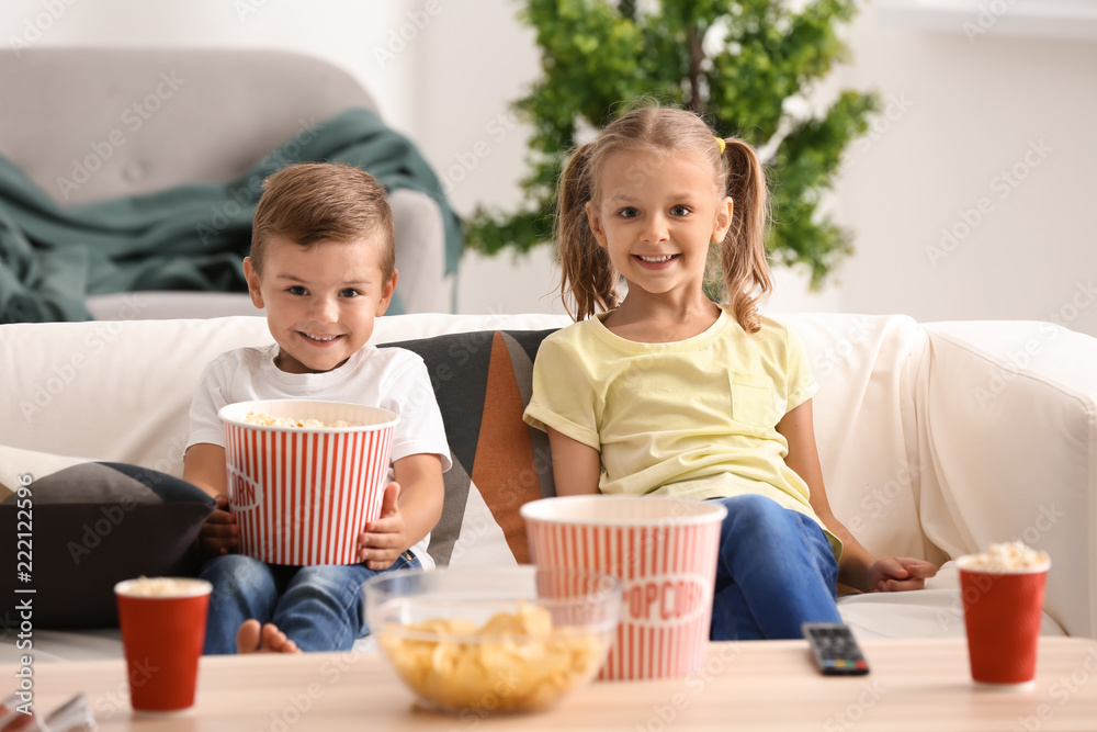 Cute children eating popcorn while watching TV at home