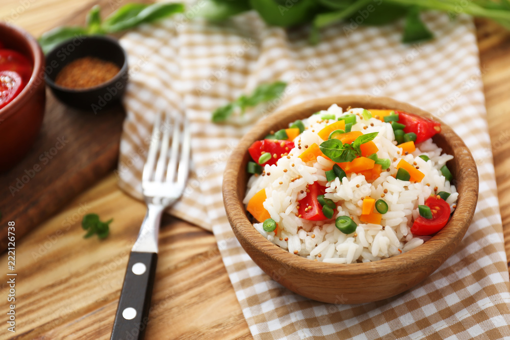 Bowl with tasty boiled rice and vegetables on wooden table