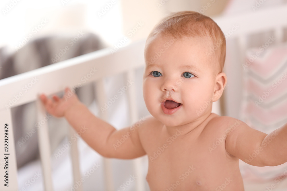 Cute little baby sitting in crib at home