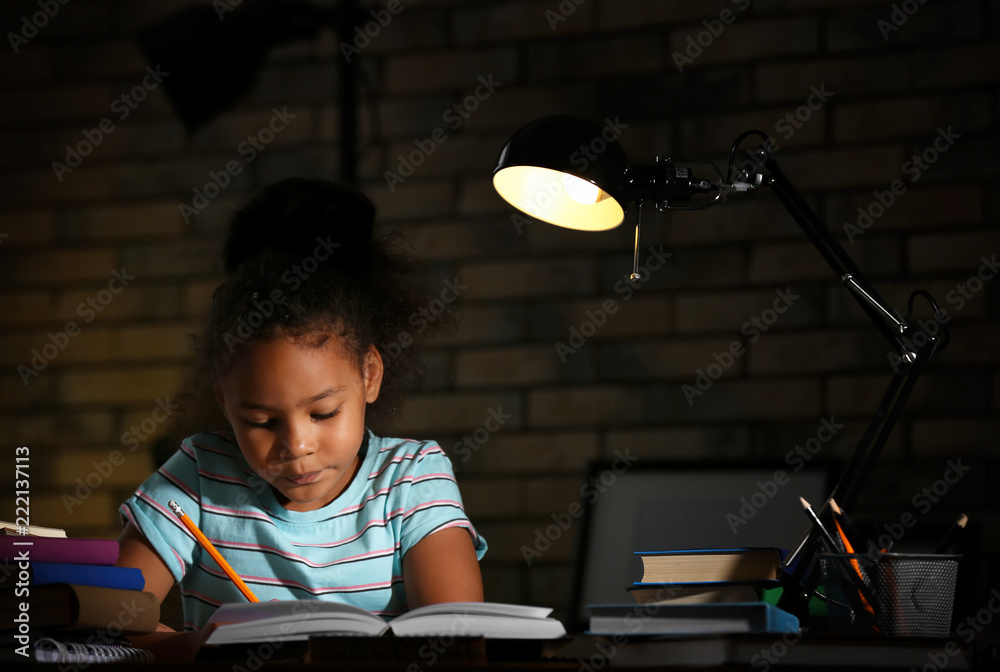 Little African-American girl doing homework in evening at home