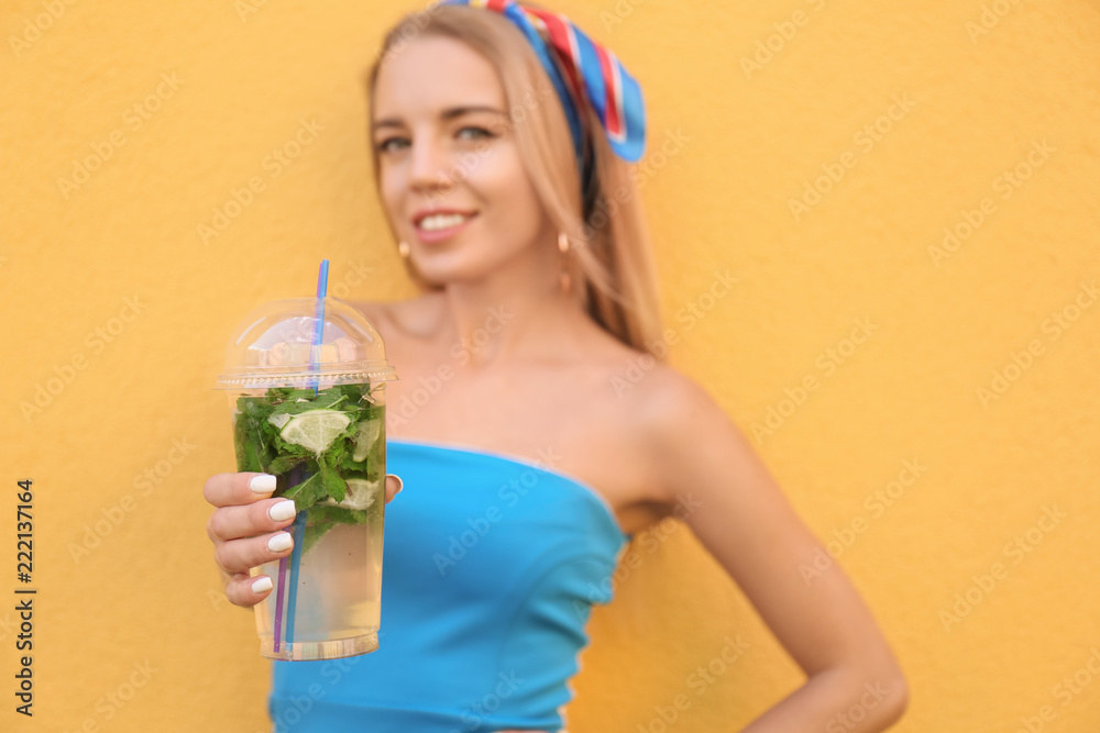 Beautiful young woman with plastic cup of fresh cocktail on color background