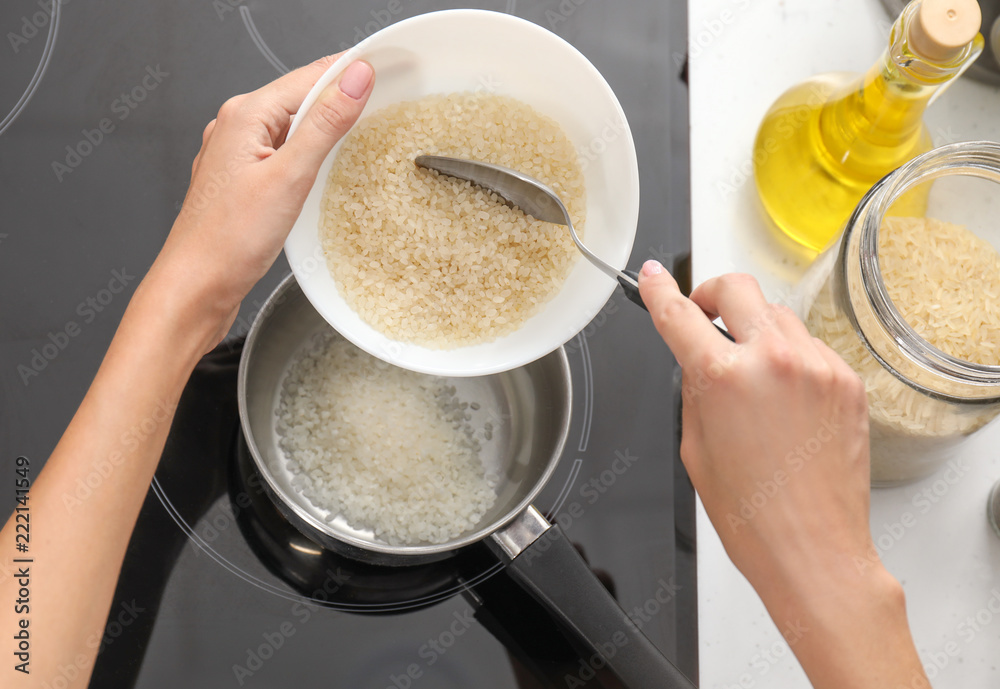 Woman pouring raw rice into saucepan with boiling water on stove