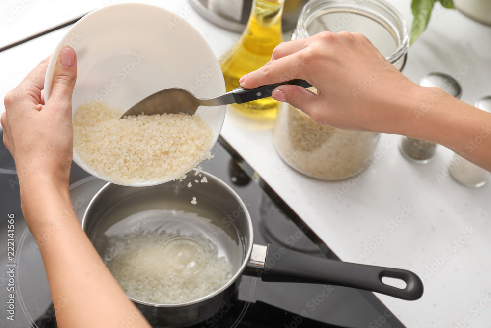 Woman pouring raw rice into saucepan with boiling water on stove