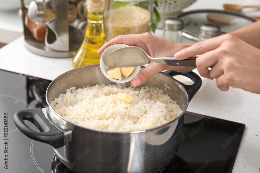 Woman adding butter into saucepan with boiled rice in kitchen