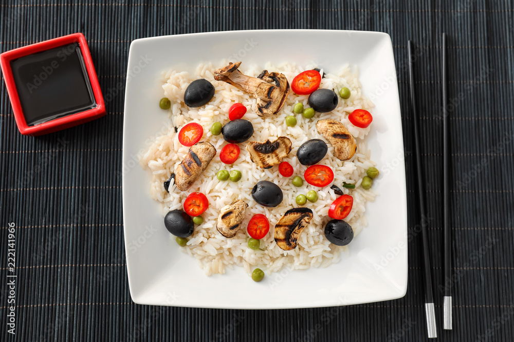 Plate with tasty boiled rice and vegetables on bamboo mat