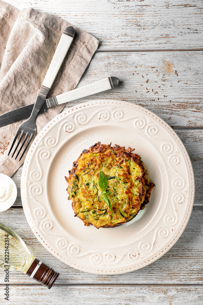 Plate with zucchini pancakes on wooden table