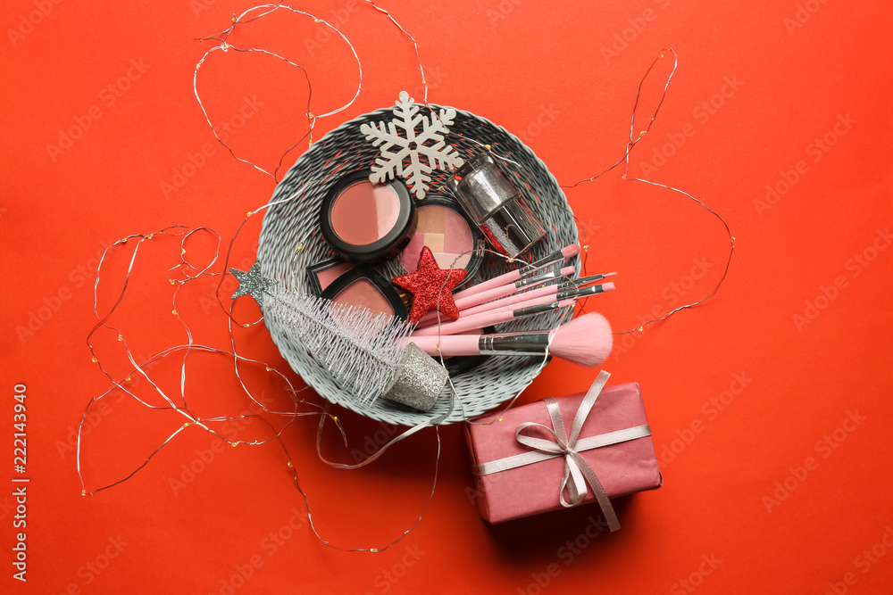 Wicker bowl with cosmetics and Christmas present on color background