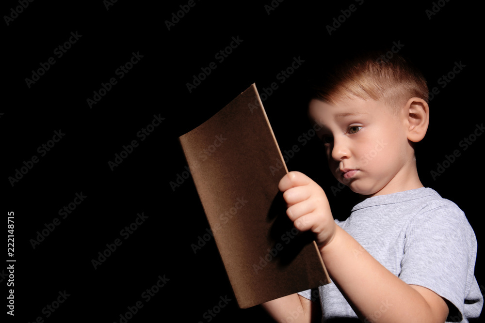 Shocked little boy reading book on dark background