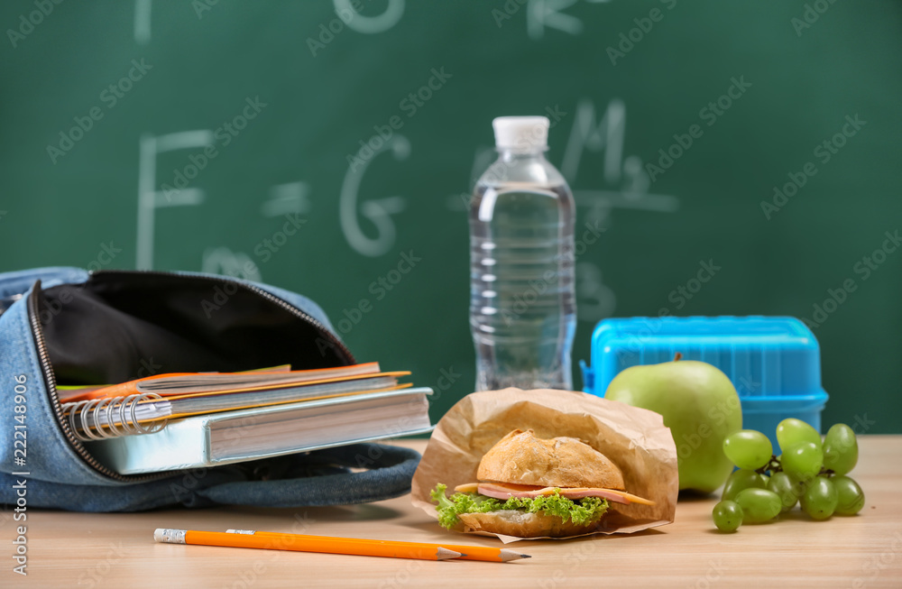 Bag with notebooks and appetizing food on table in classroom