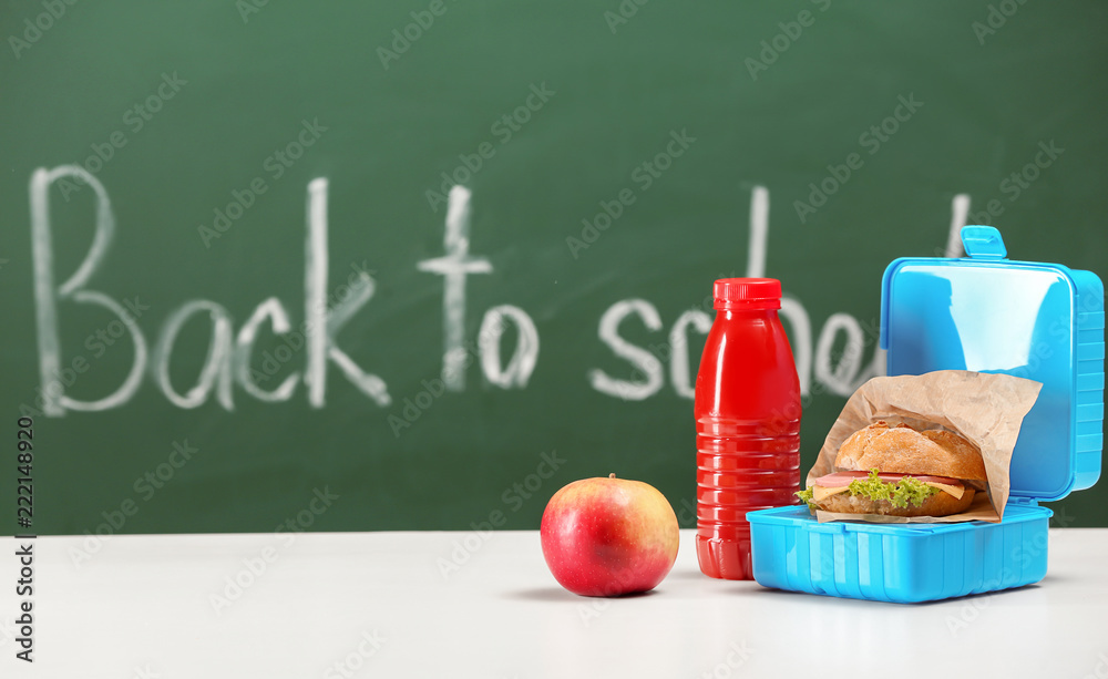 Lunch box with appetizing food and bottle of juice on white table in classroom