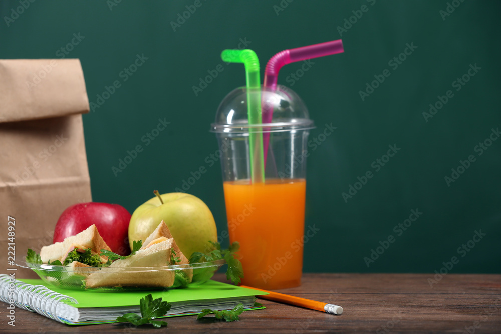 Plate with appetizing food for schoolchild and plastic cup of juice on wooden table