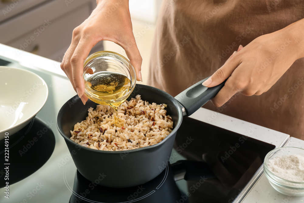 Woman pouring oil into saucepan with boiled rice on stove