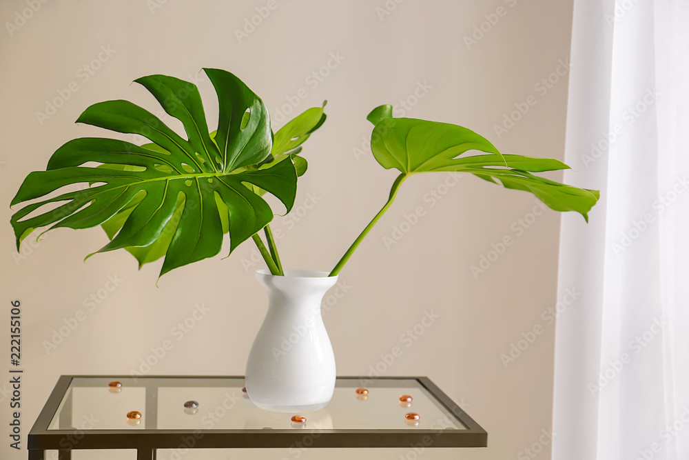 Vase with tropical leaves on glass table in room