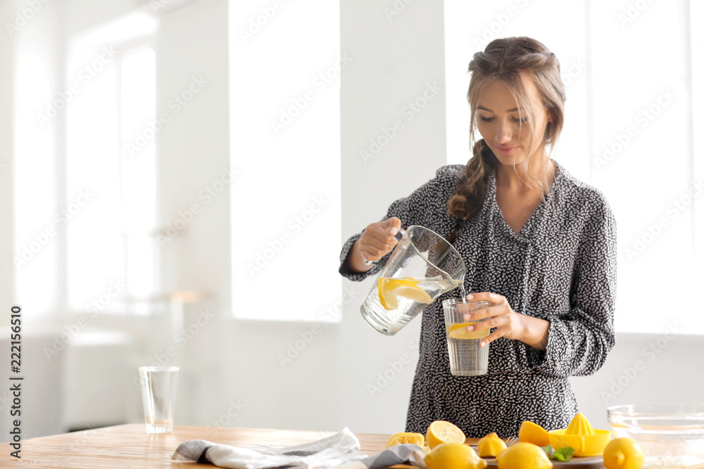 年轻女子在家里把新鲜的柠檬水从罐子里倒进杯子里