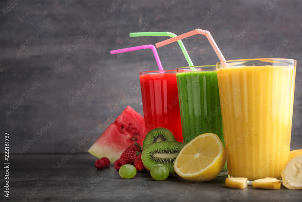 Glasses of tasty smoothies with fruits on grey table