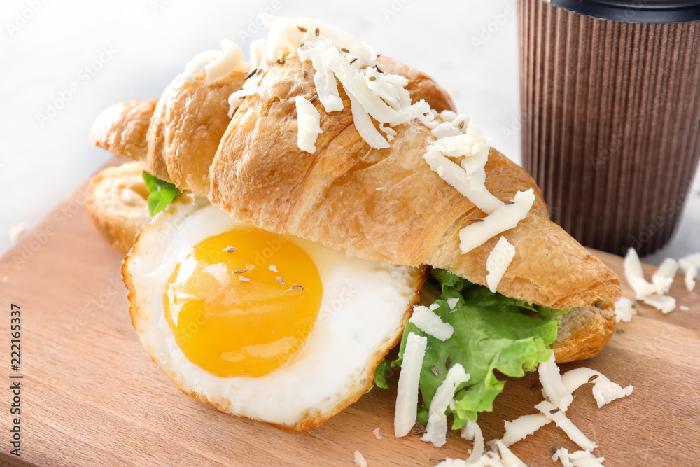 Tasty croissant sandwich with fried egg on wooden board, closeup