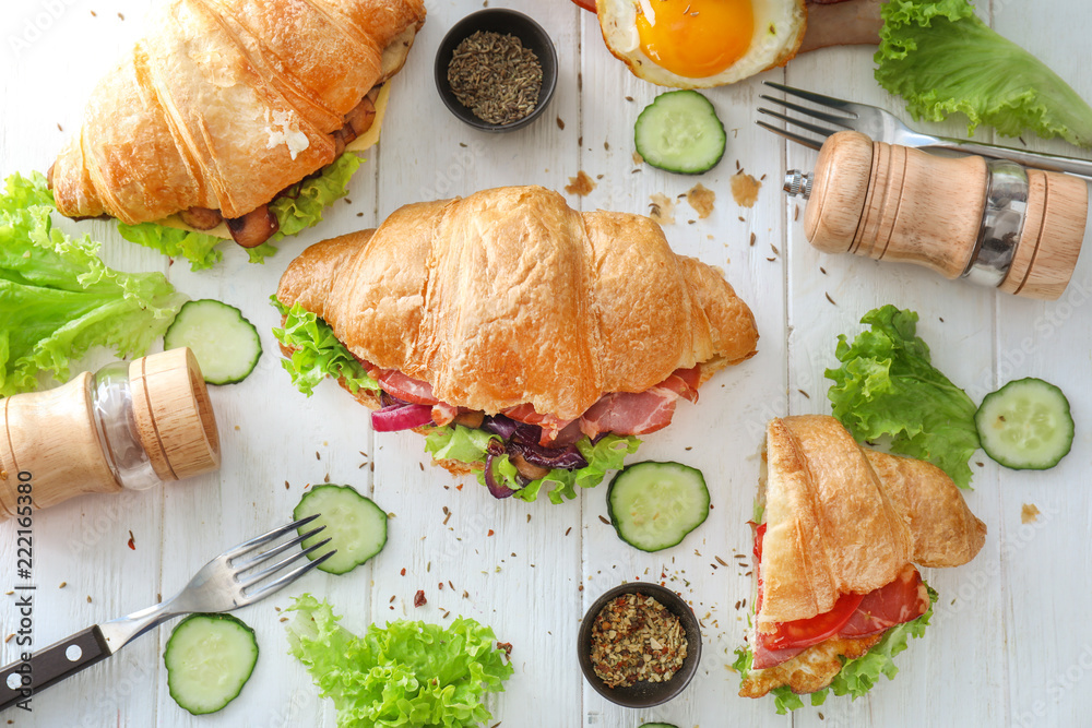 Tasty croissant sandwiches with meat and vegetables on wooden table