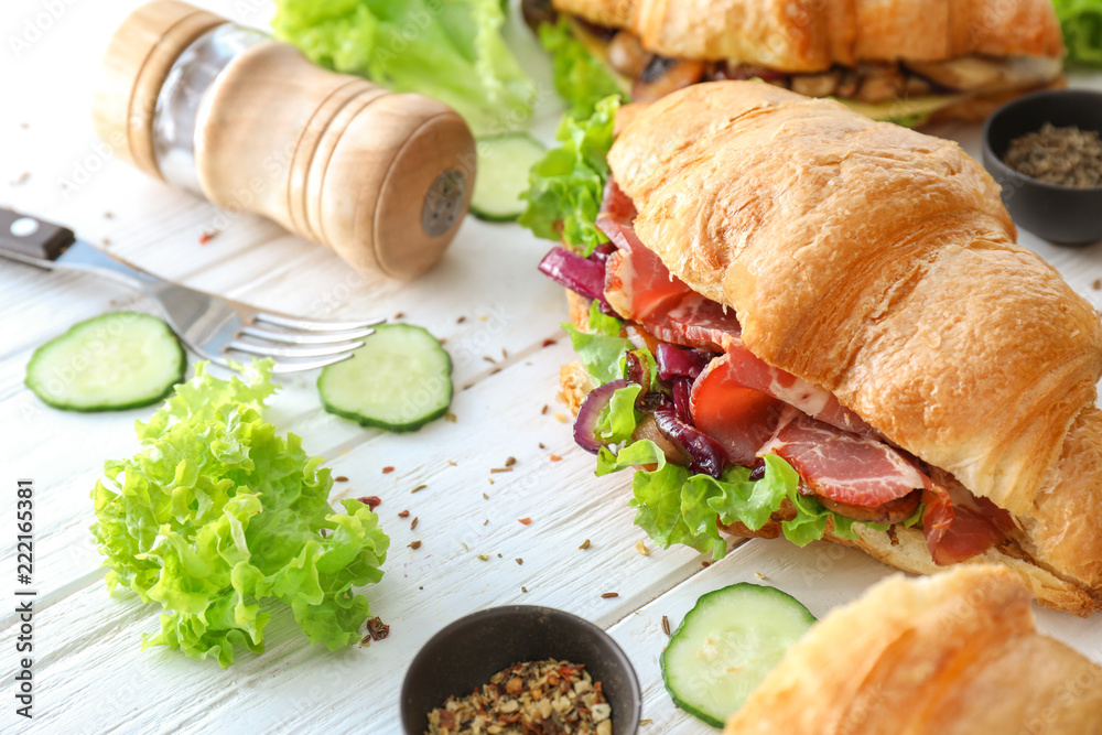 Tasty croissant sandwich with meat on white wooden table