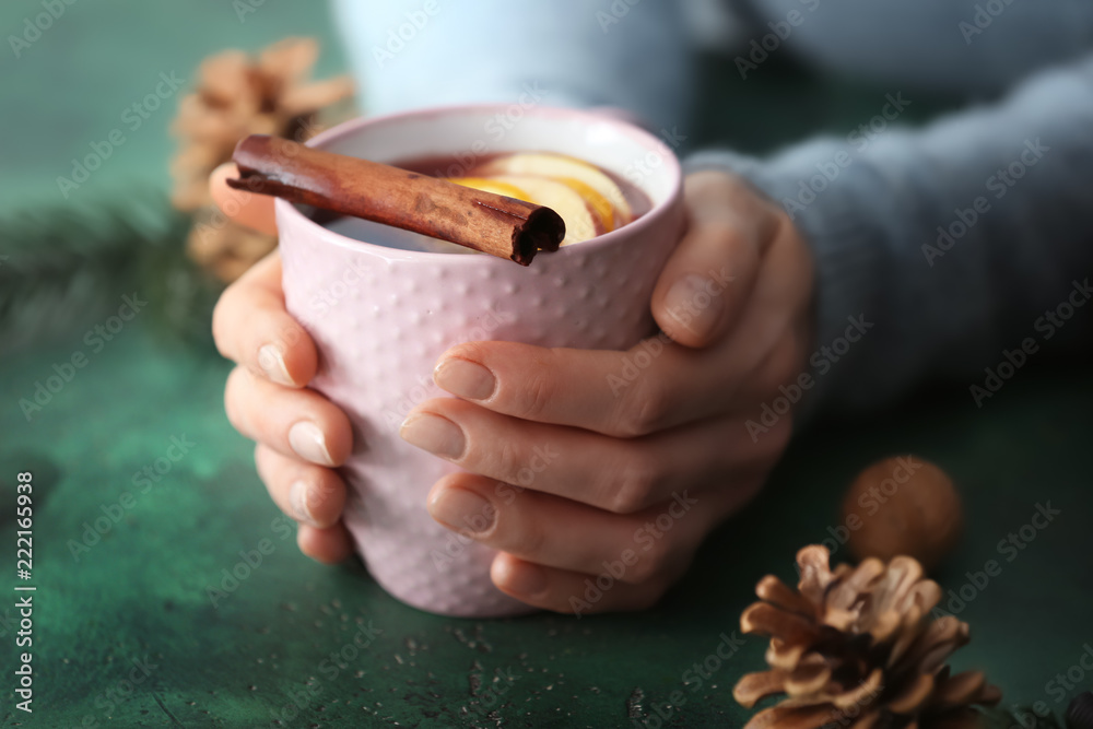 女人拿着一杯美味的热葡萄酒放在彩色桌子上，特写