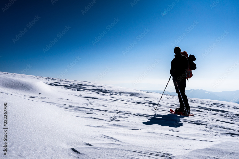 背着双肩包的男人穿着雪地鞋在冬天的风景中行走的剪影。在雪地里远足，雪